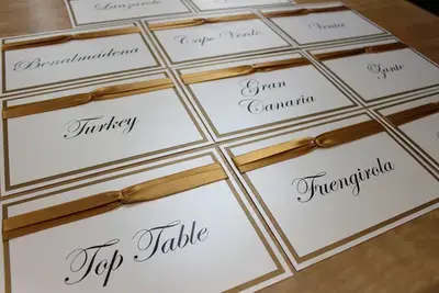 An example of a wedding table name card order made in gold and cream card with a gold satin ribbon